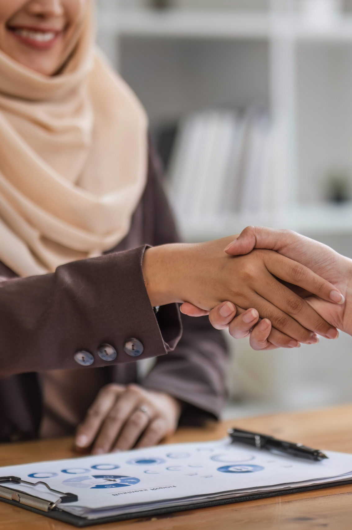 Primrose Watson Businesswomen Businesswoman wearing hijab shaking hands with another businesswoman.